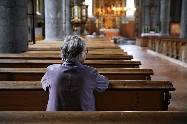 Older woman praying in an almost empty church. Shallow DOF, focus is on the woman